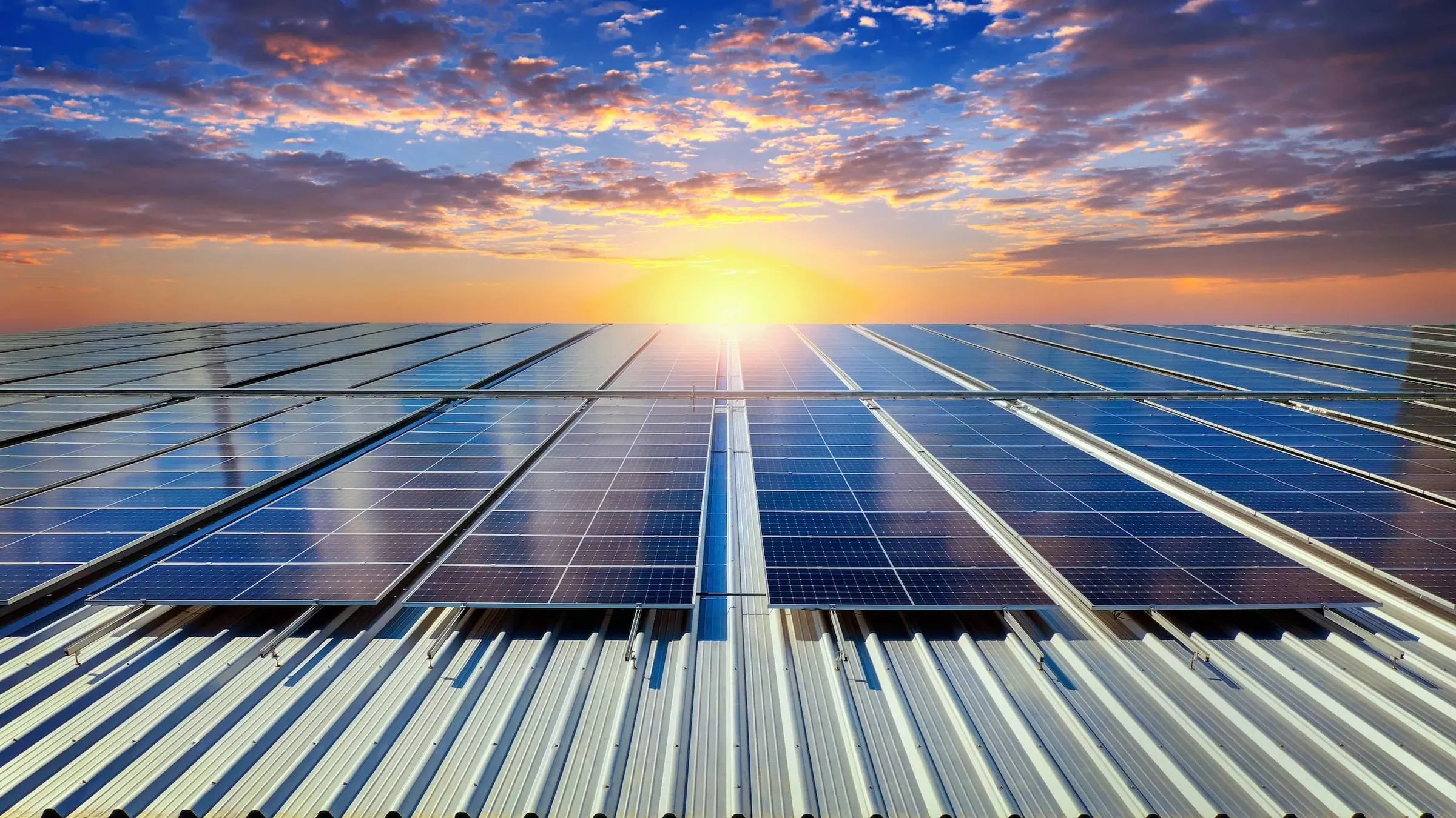 Fotovoltaické panely na střeše firemního objektu při západu slunce.